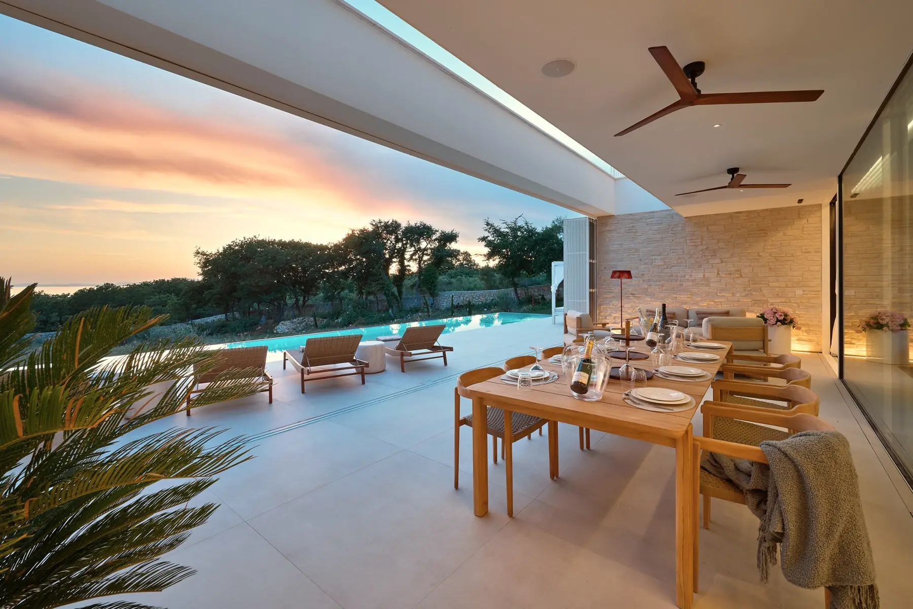 The terrace table laid for dinner at dusk, the pool and a pink sky beyond