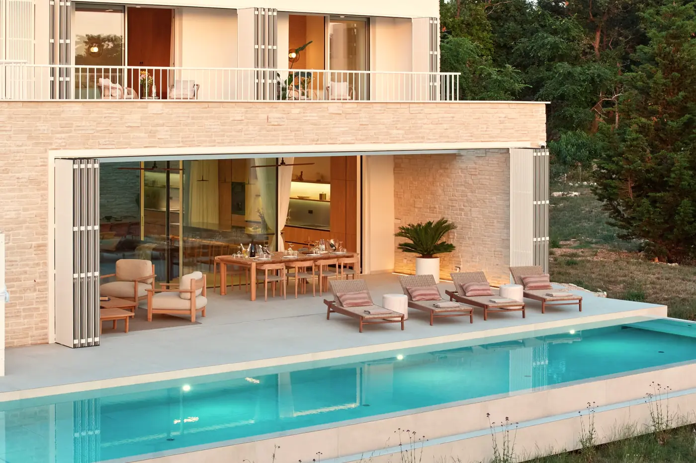 The stone facade, covered terrace and pool at dusk