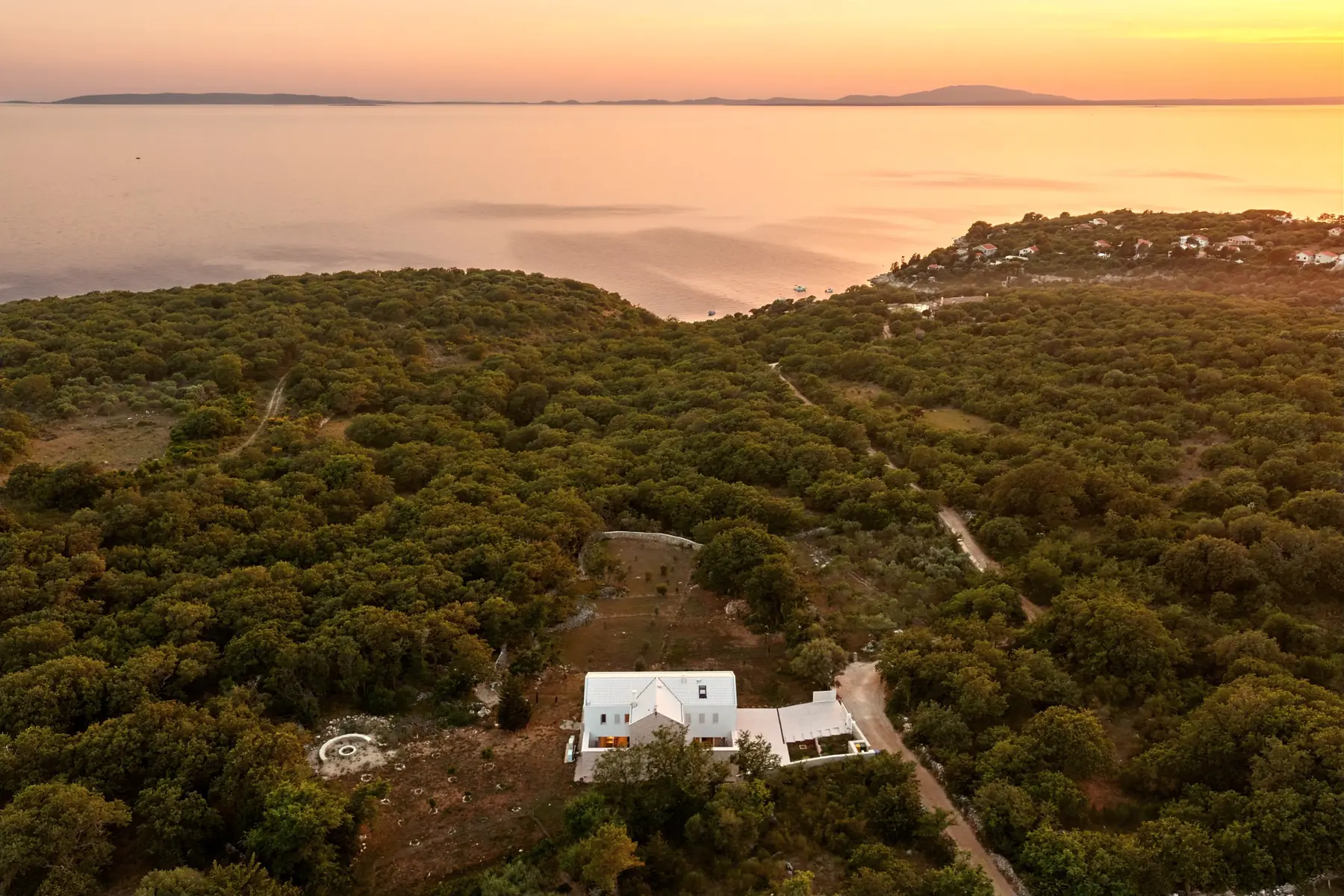 Sunset over the channel from above: the white house among oak woods, islands on the horizon